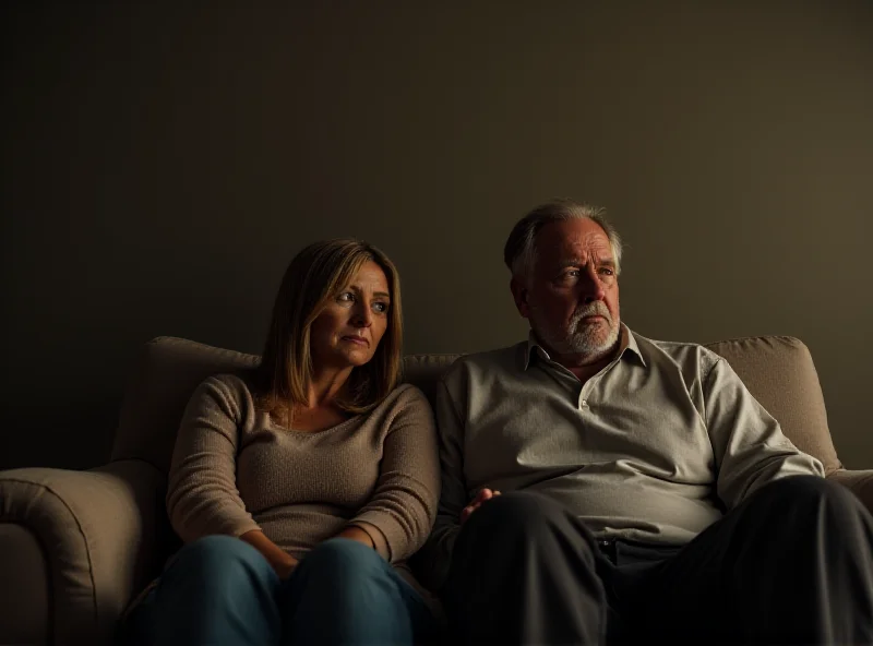 A couple sitting on a couch, looking somber and distant from each other.