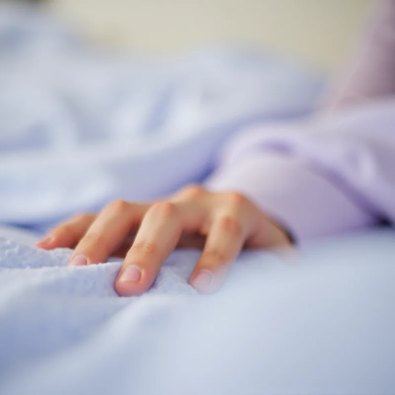 Close-up of a hand touching a soft, pastel-colored sheet set on a bed, highlighting the texture and comfort.