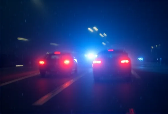 A blurred image of a road accident scene with flashing police lights at night.