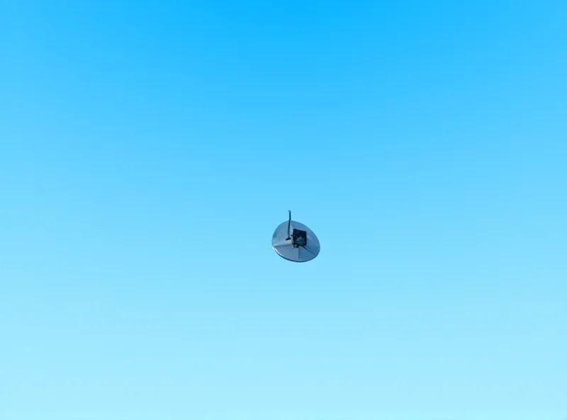 A satellite dish pointed towards the sky, with a clear blue sky in the background.