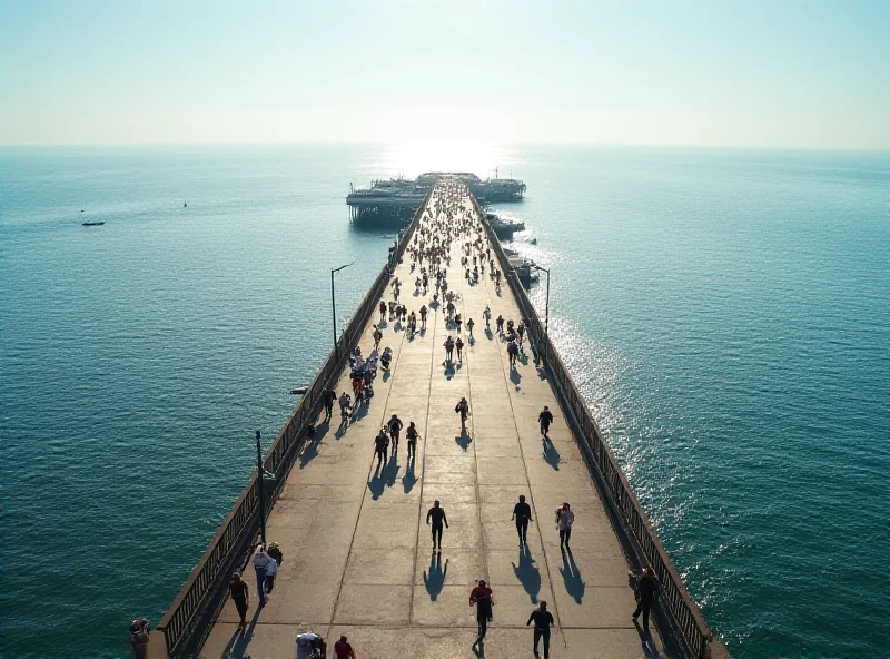 A long pier stretching far out into the ocean, with people walking and enjoying the view. The sky is clear and blue, and the water is calm and inviting.